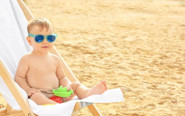 Anak kecil duduk di kursi pantai di pantai — Stok Foto