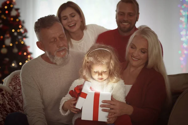 Cute little girl with her family opening Christmas gift box at home