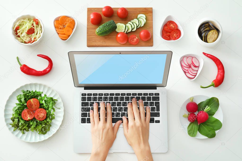 Woman using laptop near vegetables on white background. Food blogger concept