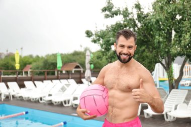 Yakışıklı genç adam topu ayakta yakınındaki Yüzme Havuzu ile