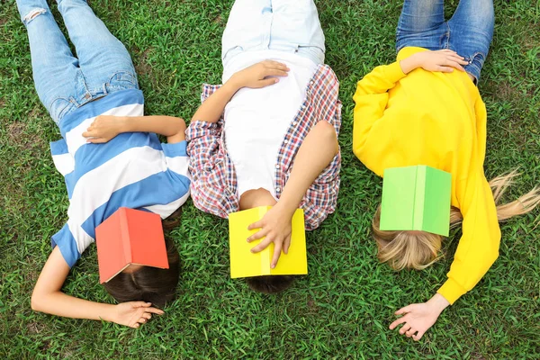 Adolescentes com livros deitados na grama verde — Fotografia de Stock