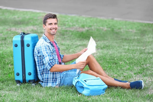 Молодий чоловік з картою сидить на зеленій траві на відкритому повітрі — стокове фото
