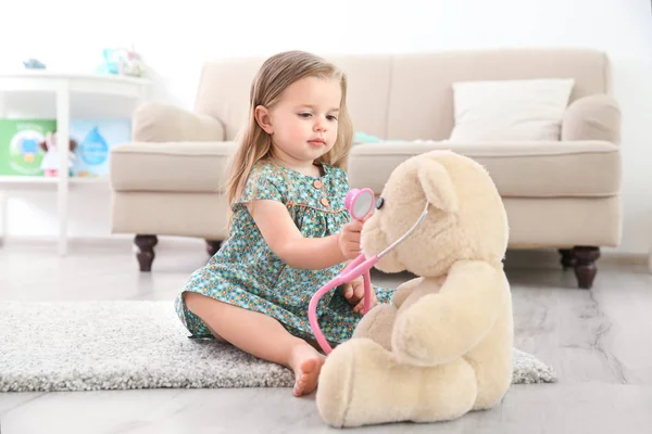 可爱的小女孩与听诊器和玩具熊玩在家里 — 图库照片