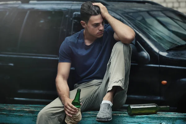Чоловік сидить з пляшкою алкоголю біля машини — стокове фото