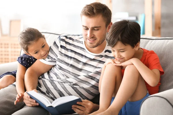 Jovem e seus filhos lendo livro em casa — Fotografia de Stock