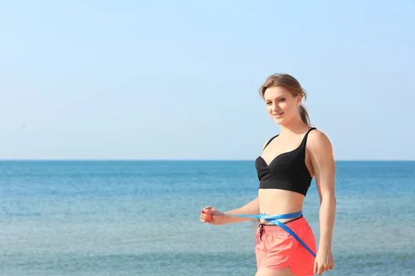 Joven mujer deportiva que mide la cintura en la playa del mar — Foto de Stock