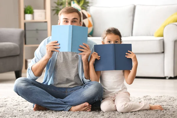 Young man and his little daughter playing with books at home