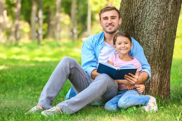 Young man and his little daughter reading book in park — Stock Photo, Image