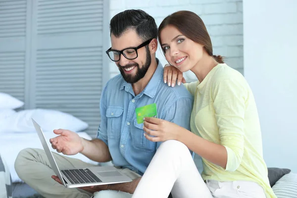 Νεαρό ζευγάρι με φορητό υπολογιστή και την πιστωτική κάρτα στο σπίτι. Έννοια αγορών στο διαδίκτυο — Φωτογραφία Αρχείου