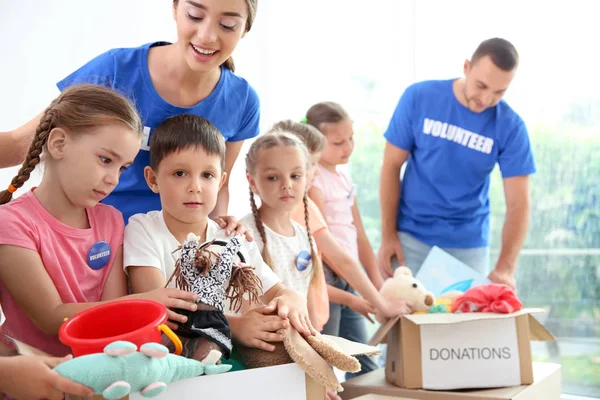 Szczęśliwy wolontariuszy z dziećmi sortowanie Darowizna towarów wewnątrz — Zdjęcie stockowe