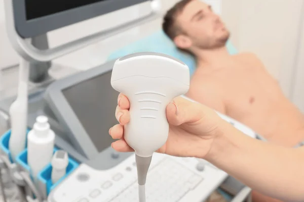 Hand van arts met een echografie apparatuur en wazig patiënt op achtergrond — Stockfoto