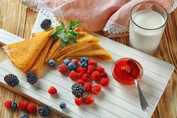 Board with tasty thin pancakes and berries on table — Stock Photo, Image