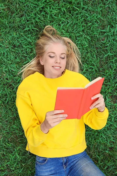 Adolescente chica leyendo libro mientras está acostado en la hierba verde — Foto de Stock