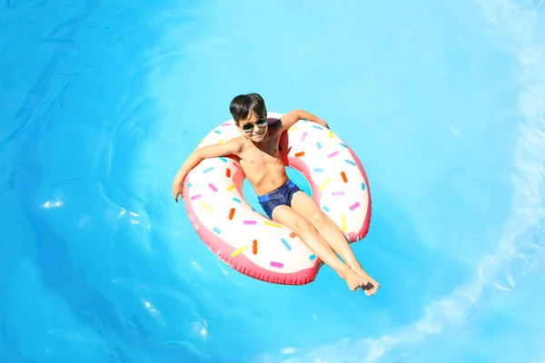 Menino bonito com donut inflável na piscina — Fotografia de Stock