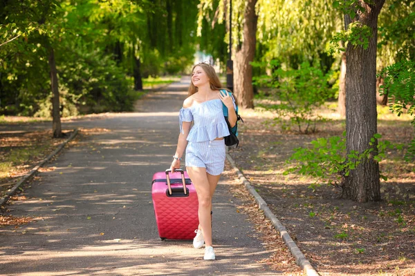 Beautiful young tourist with suitcase in park — Stock Photo, Image
