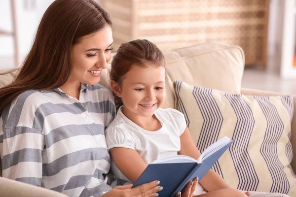 Mujer joven y su hija pequeña leyendo libro en casa — Foto de Stock