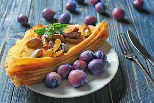 Assiette avec de savoureuses crêpes fines et des prunes sur la table — Photo