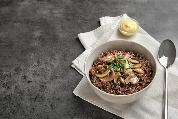 Tigela com delicioso arroz vermelho e cogumelos na mesa — Fotografia de Stock