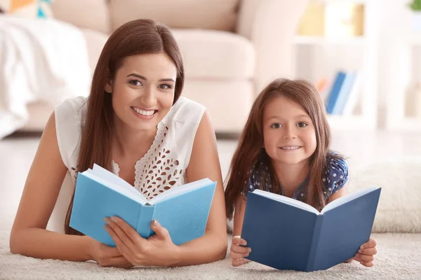 Mujer joven y su hija pequeña leyendo libros en casa — Foto de Stock