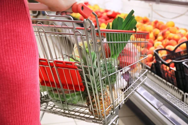 Jonge vrouw met een winkelwagentje in de supermarkt — Stockfoto