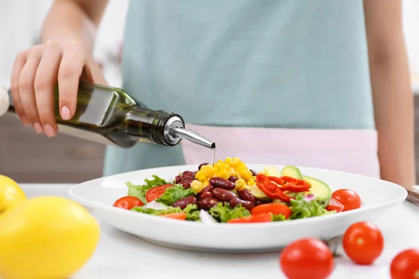 Женщина наливает оливковое масло в салат — стоковое фото