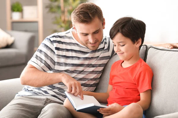 Молодой человек и его маленький сын читают дома книгу — стоковое фото