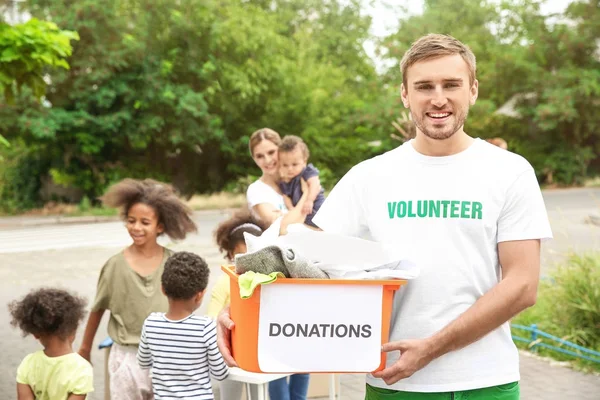 Young male volunteer holding box of donations outdoors — Stock Photo, Image