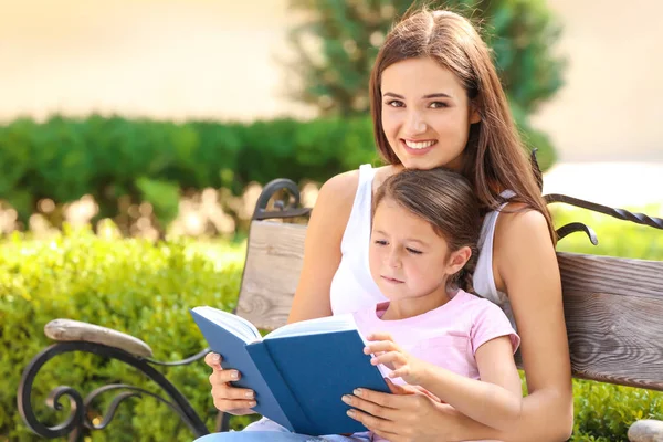 Fiatal nő, és vele a kis lányom olvasó könyv park — Stock Fotó