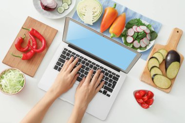 Beyaz arka plan üzerinde sebze yakınındaki dizüstü kullanan kadın. Gıda blogger kavramı