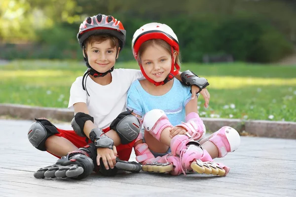 Alegre menino e menina em patins sentados no parque — Fotografia de Stock