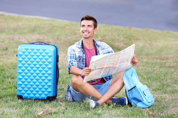 Jeune homme avec carte assis sur l'herbe verte à l'extérieur — Photo