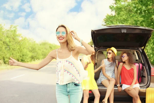 Jovem mulher com seus amigos carona na estrada — Fotografia de Stock