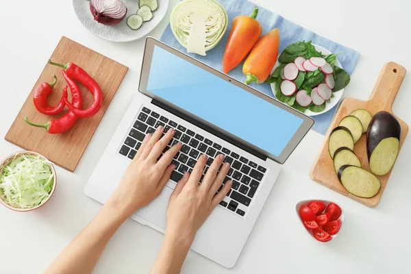 Kvinna med laptop nära grönsaker på vit bakgrund. Blogger matkoncept — Stockfoto