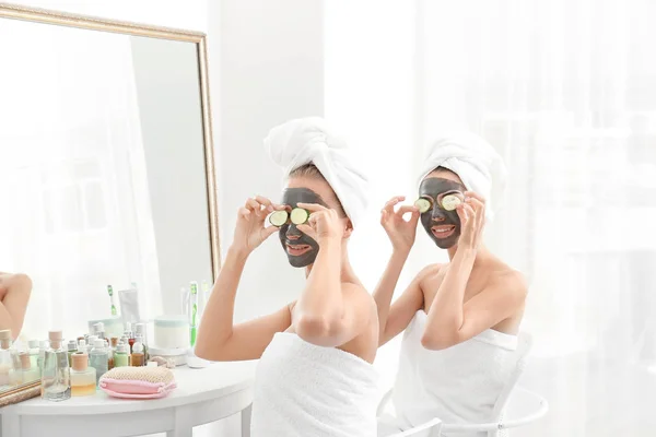 Mujeres jóvenes con máscaras faciales y rodajas de pepino en el baño —  Fotos de Stock
