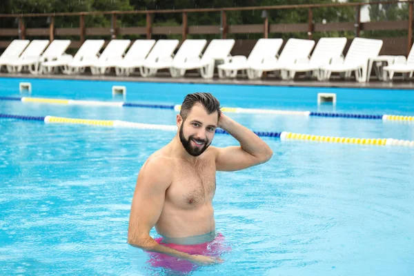 Schöner junger Mann entspannt sich im blauen Swimmingpool — Stockfoto