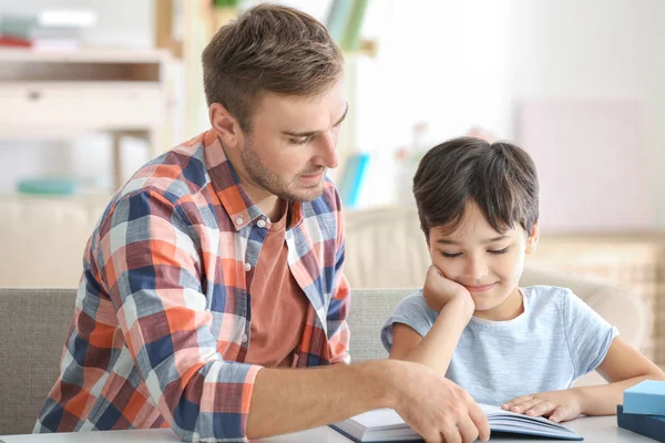 Joven y su pequeño hijo leyendo libro en casa — Foto de Stock