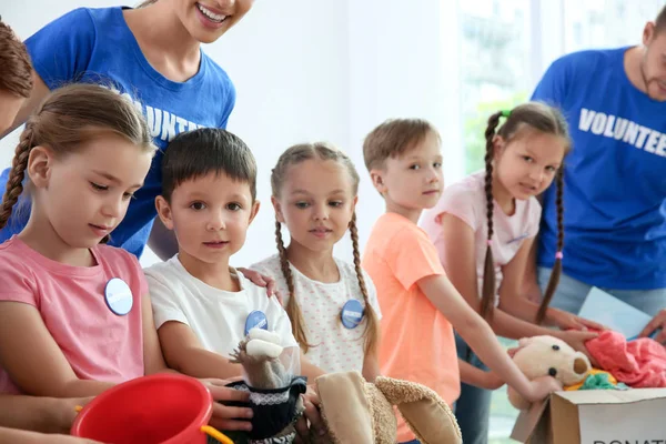 Volontari felici con bambini che selezionano beni da donare al chiuso — Foto Stock