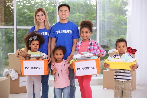 Jóvenes voluntarios y niños pequeños con cajas de donaciones en la sala de luz. Voluntariado en el extranjero concepto — Foto de Stock