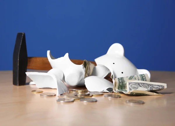 Martelo e quebrado porquinho banco com dinheiro na mesa contra fundo de cor — Fotografia de Stock
