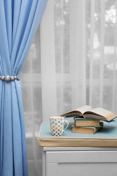 Zachte bank met boeken en koffie in de buurt van mooie gordijnen binnenshuis — Stockfoto