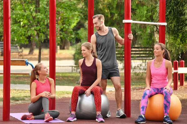 Mujeres jóvenes haciendo ejercicio con entrenador personal en el campo de deportes —  Fotos de Stock