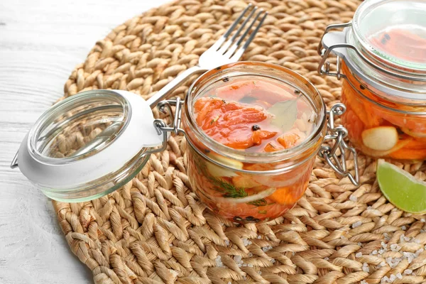 Jar with delicious marinated salmon on wicker mat — Stock Photo, Image