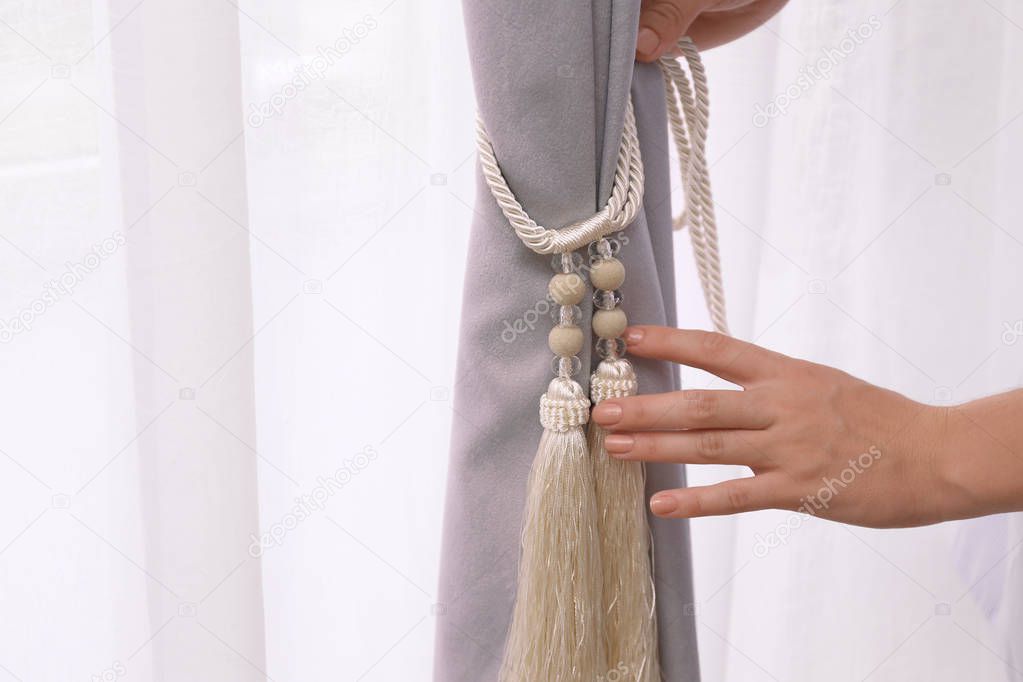 Woman putting tieback on beautiful curtains indoors, closeup