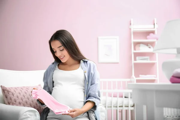Mulher grávida segurando roupas de bebê em casa — Fotografia de Stock