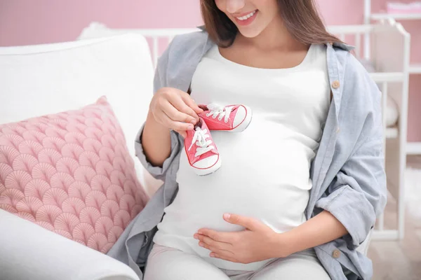 Mulher grávida segurando sapatos de bebê em casa — Fotografia de Stock