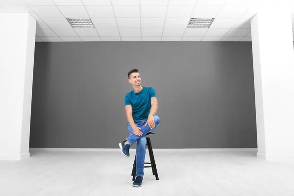 Young man sitting on stool in empty room — Stock Photo, Image