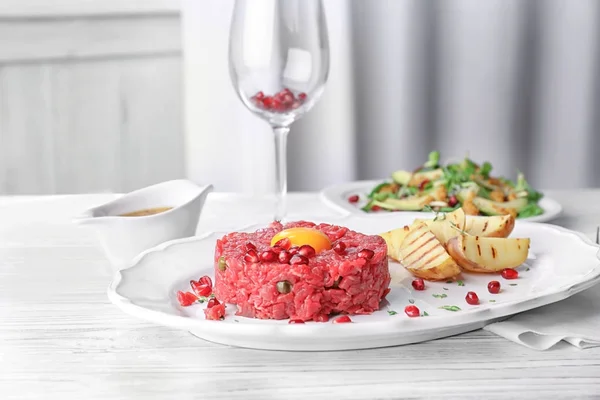 Delicioso tártaro de bistec con yema, semillas de granada y patatas en el plato —  Fotos de Stock