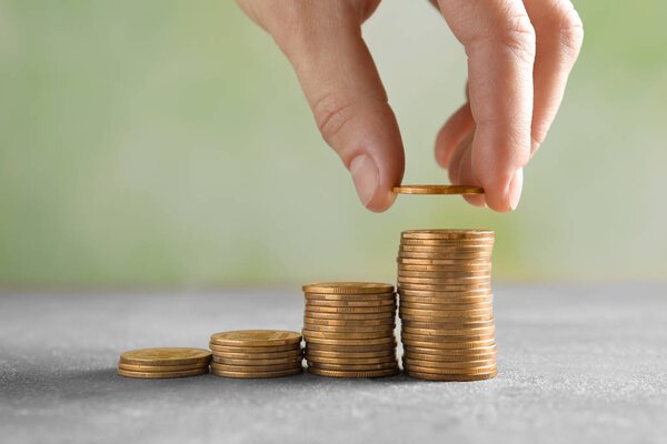 Woman stacking coins on blurred background, closeup