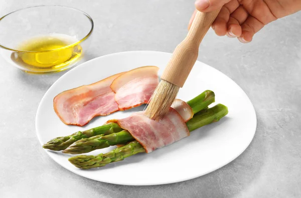 Mujer aplicando aceite sobre el tocino envuelto espárragos —  Fotos de Stock