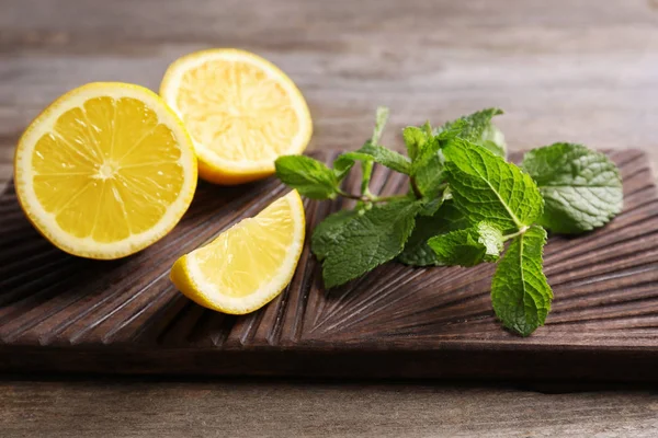 Cutting board with mint and lemon on wooden background — Stock Photo, Image